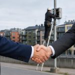 Två affarsfolk skakar hand i forgrund medan en obrandad fiberbox syns i bakgrunden